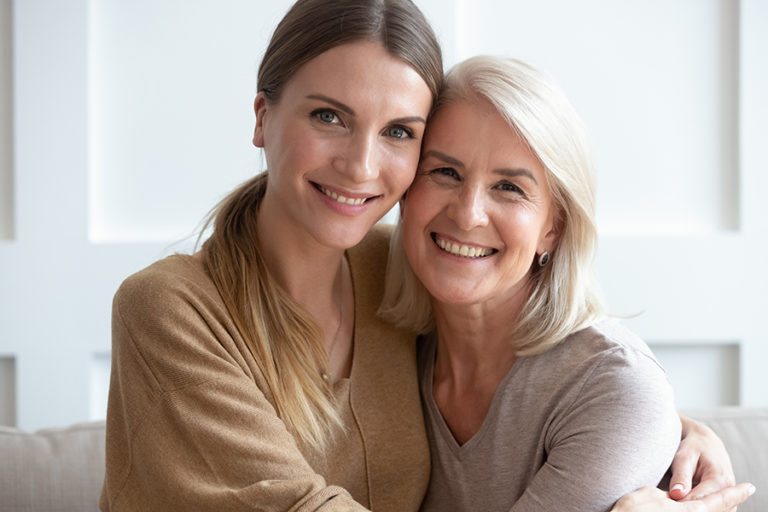 Close up image aged mother adult daughter sitting on couch indoors smiling looking posing for camera hugging feels happy spend time together, concept of love relative people, multi-generational family