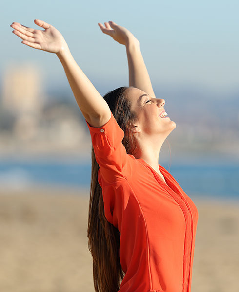 Side view portrait of a happy beautiful woman breathing and raising arms on the beach in a sunny day